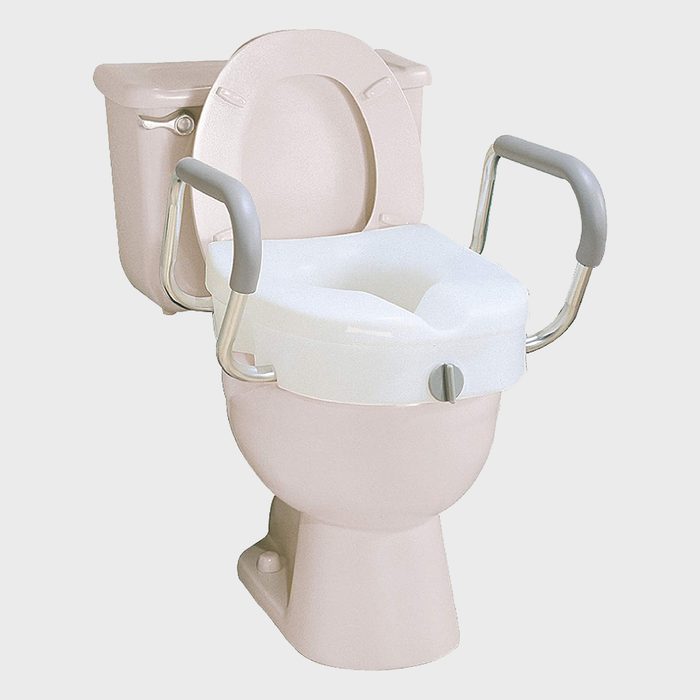 A commode features a raised toilet seat with armrests, enabling easier use in a bathroom setting for individuals requiring assistance.
