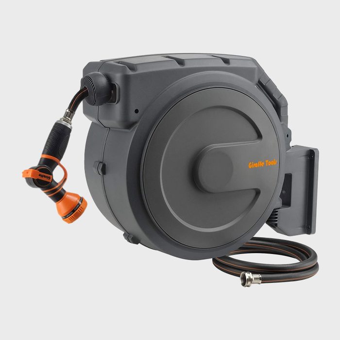 A wall-mounted hose reel stores a coiled garden hose. The nozzle is attached, ready for watering plants in an outdoor setting.