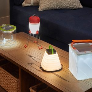 A table displays four portable lamps, illuminating the wooden surface, with a dark couch in the background, creating a cozy indoor ambiance.