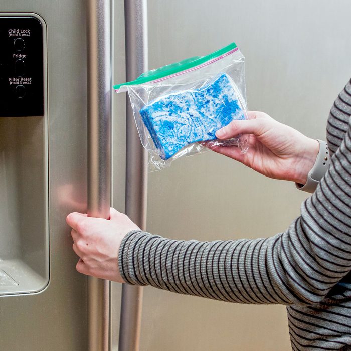 person holding a sponge for a homemade ice pack inside a plastic ziplock bag standing near refrigerator doors