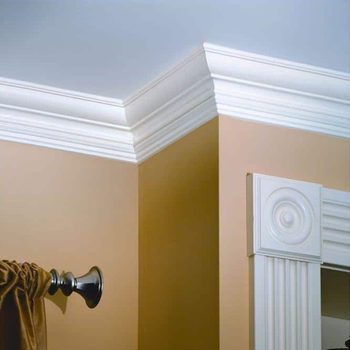 White crown molding connects two walls at a corner, enhancing an interior space with a cream-colored wall and a decorative trim near a curtain rod.