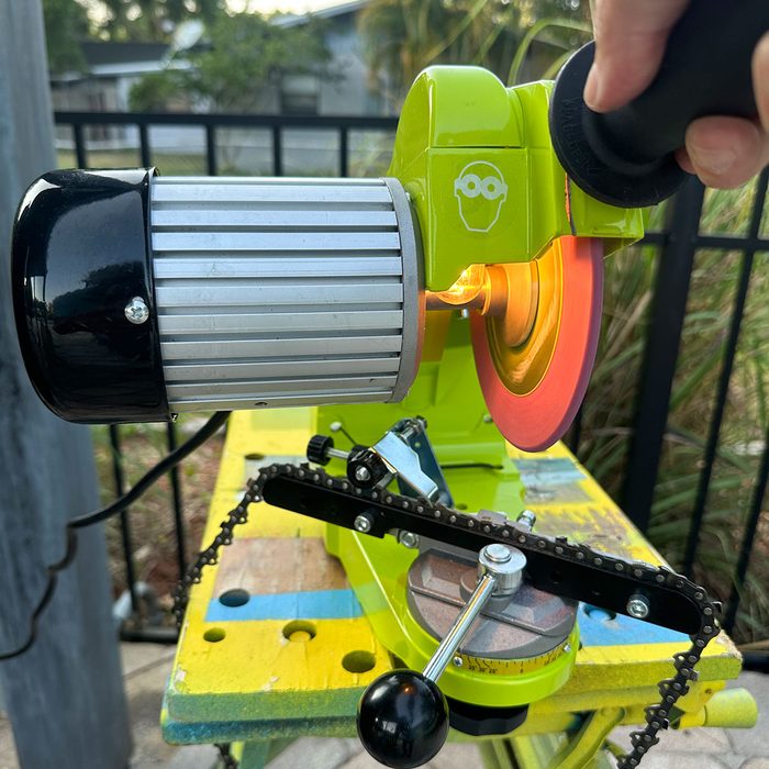 A green sharpening tool is activated, with a rotating red disc and an illuminating light, positioned on a colorful workbench in an outdoor setting.