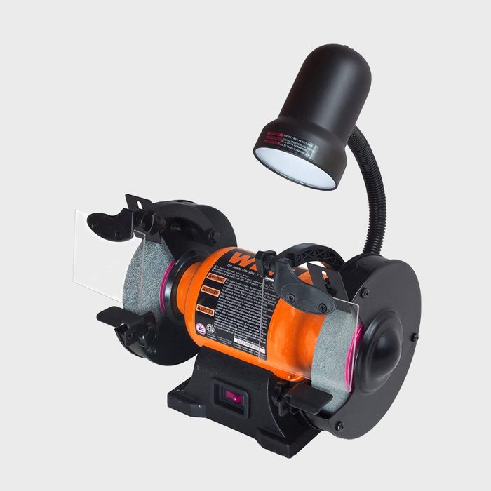 A sharpening tool with grinding wheels is running under a flexible lamp, resting on a black base, typically used for sharpening tools or blades.