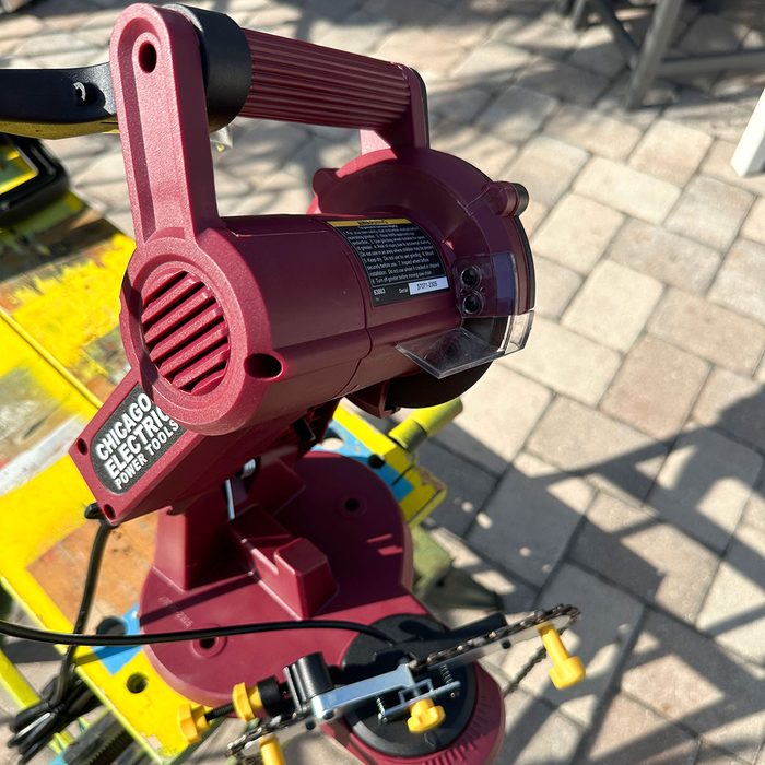 A maroon power tool is positioned on a colorful, cluttered work surface, with sunlight casting shadows over its features, ready for cutting tasks.