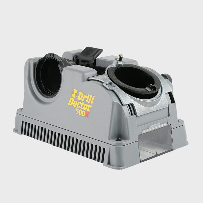 A gray drill sharpening device sits on a flat surface, with two openings for drill bits, designed for precise sharpening in a workshop environment.