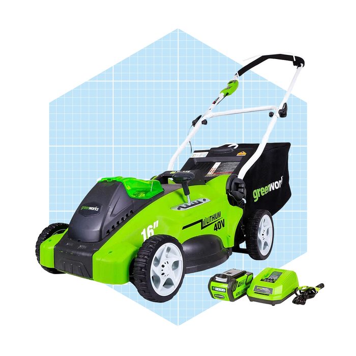 A green and black electric lawn mower stands on a blue geometric background, accompanied by two batteries and a charger, indicating a ready-to-use garden tool.