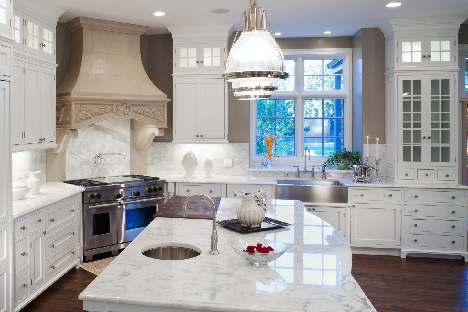 A marble kitchen countertop features a sink, vase, and decorative items, while a stove and hood adorn the wall in a bright, modern setting.