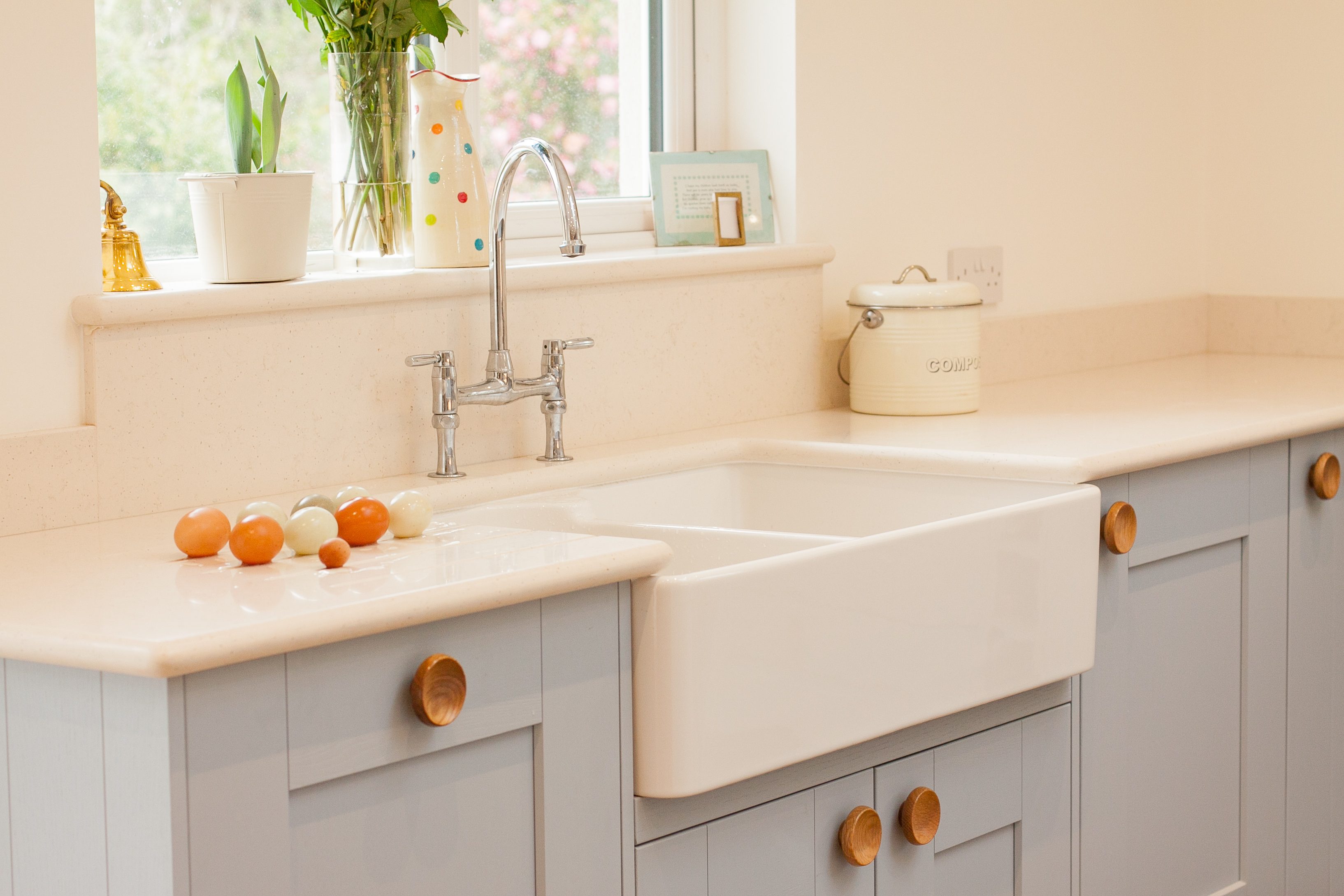 A white farmhouse sink sits on a light countertop, with various eggs arranged nearby, surrounded by a modern kitchen setting with decorative elements.
