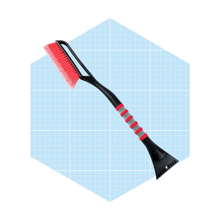 A red and black cleaning tool with bristles and a scraper is positioned diagonally against a light blue grid background.