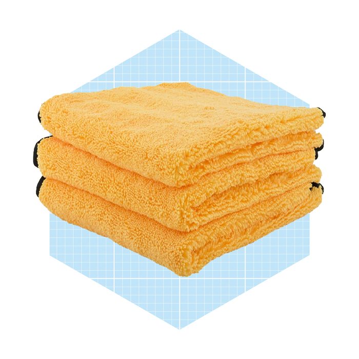 Three stacked, bright yellow microfiber towels sit on a light blue grid-patterned background, showcasing their soft texture and vibrant color.