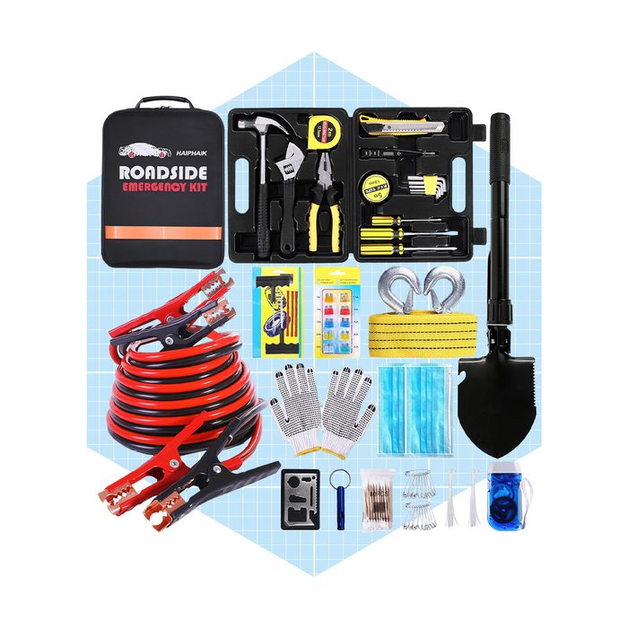 A roadside emergency kit contains tools, jumper cables, gloves, a shovel, and safety items, arranged neatly on a blue grid background.