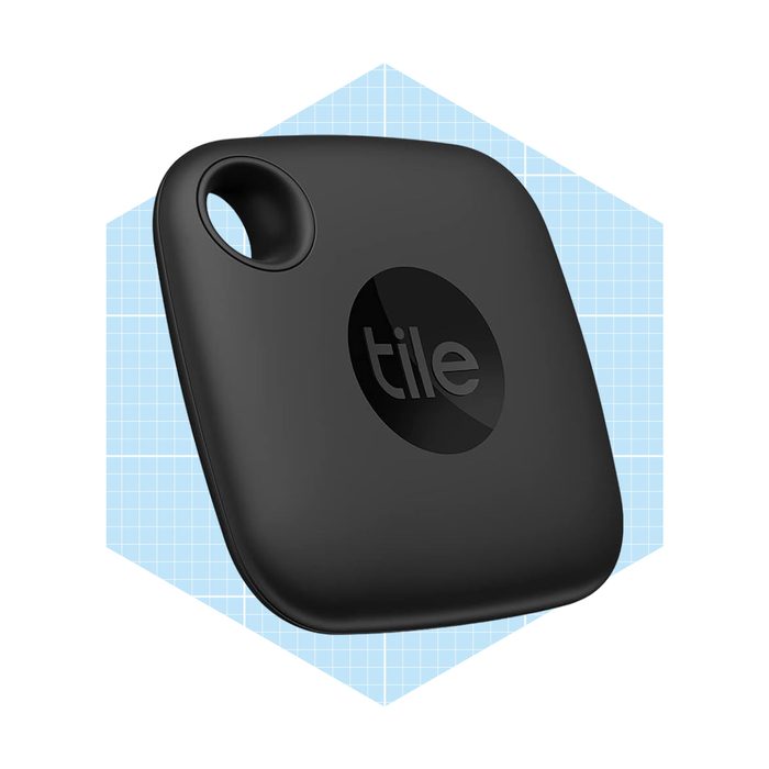 A black square tracking device with a circular logo is displayed against a light blue grid background, designed to help locate lost items.