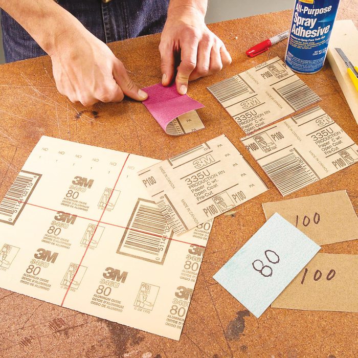 person folding sandpaper at a large workbench