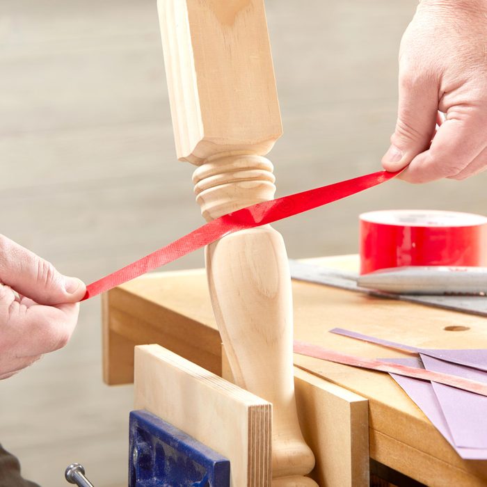 close up of person using thin piece of sand paper tape to get into small spot on a leg chair