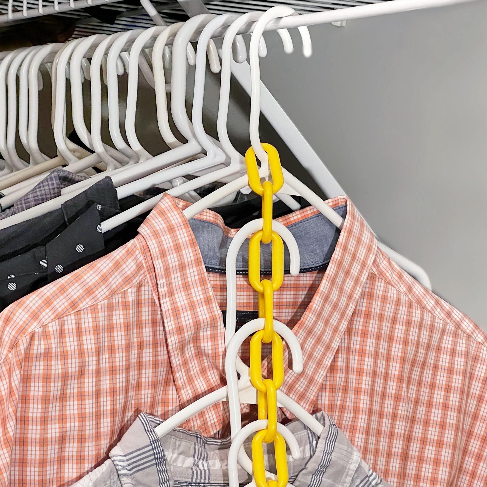 A chain of yellow plastic links holds several white hangers together, each supporting different patterned shirts, in a closet setting.