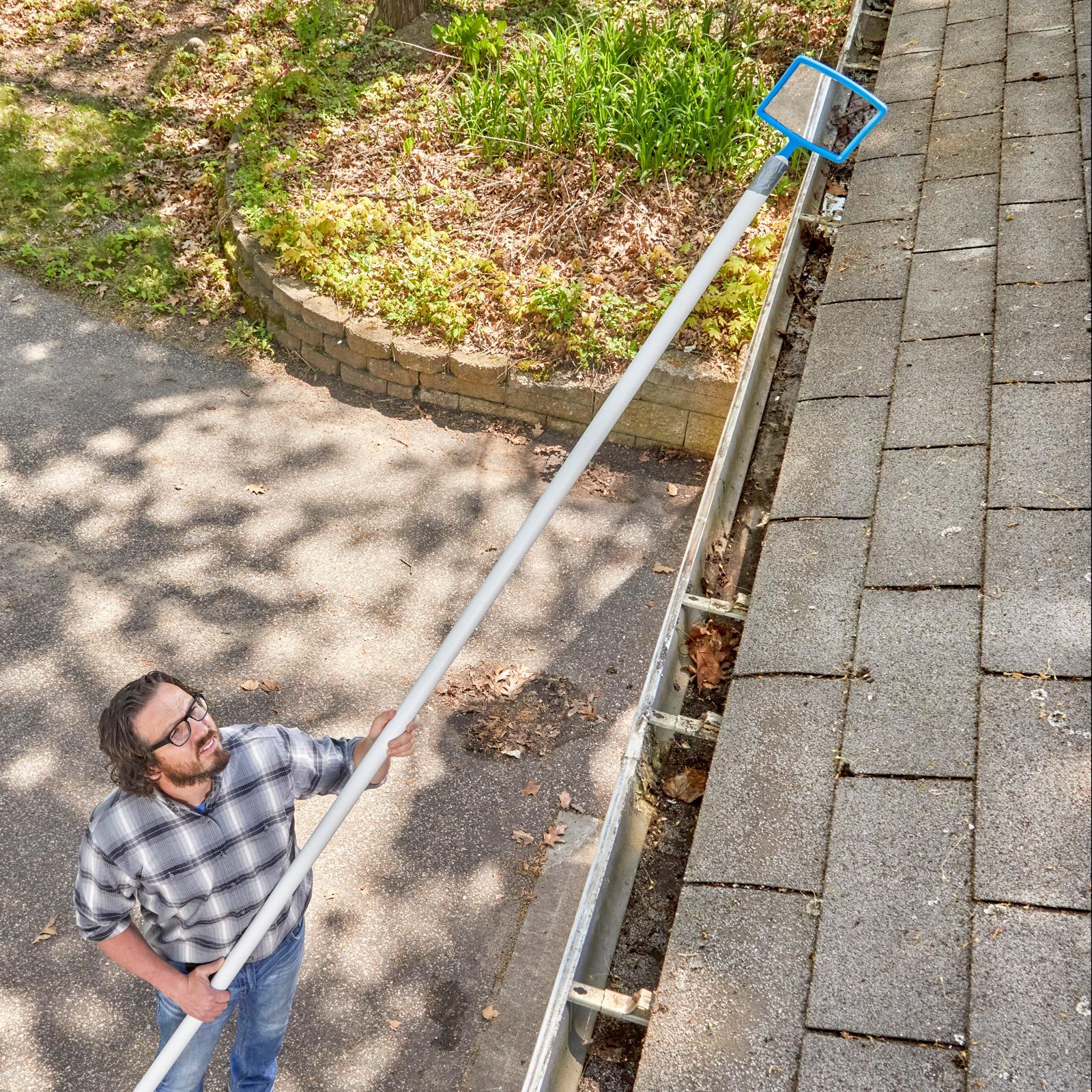 man checking gutters from the ground using a long pole with a mirror at the end