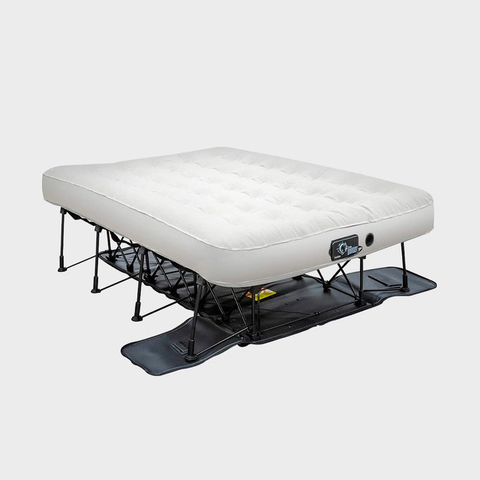 An elevated air mattress is set up on a black frame, designed for sleeping. The background is plain and light-colored.