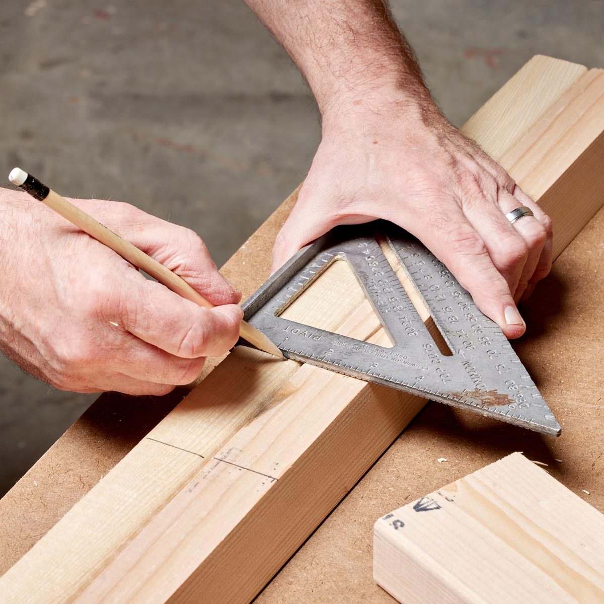 A hand uses a pencil to mark a wooden plank against a metal square on a workbench, surrounded by other pieces of wood.