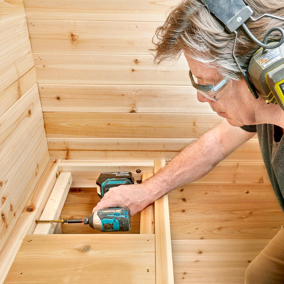 A person uses a battery-powered drill to secure wood pieces together. The environment features wooden panels, suggesting an indoor construction or woodworking setting.