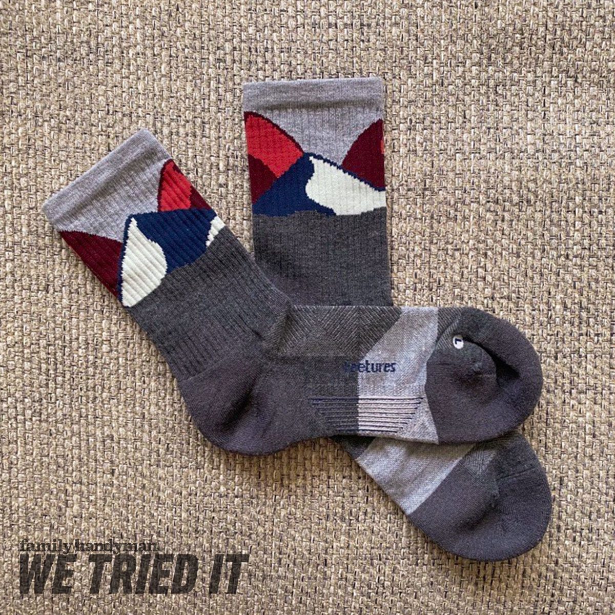 Colorful patterned socks lay on a textured surface, showcasing mountain designs. The socks display a mix of gray, red, blue, and white colors.