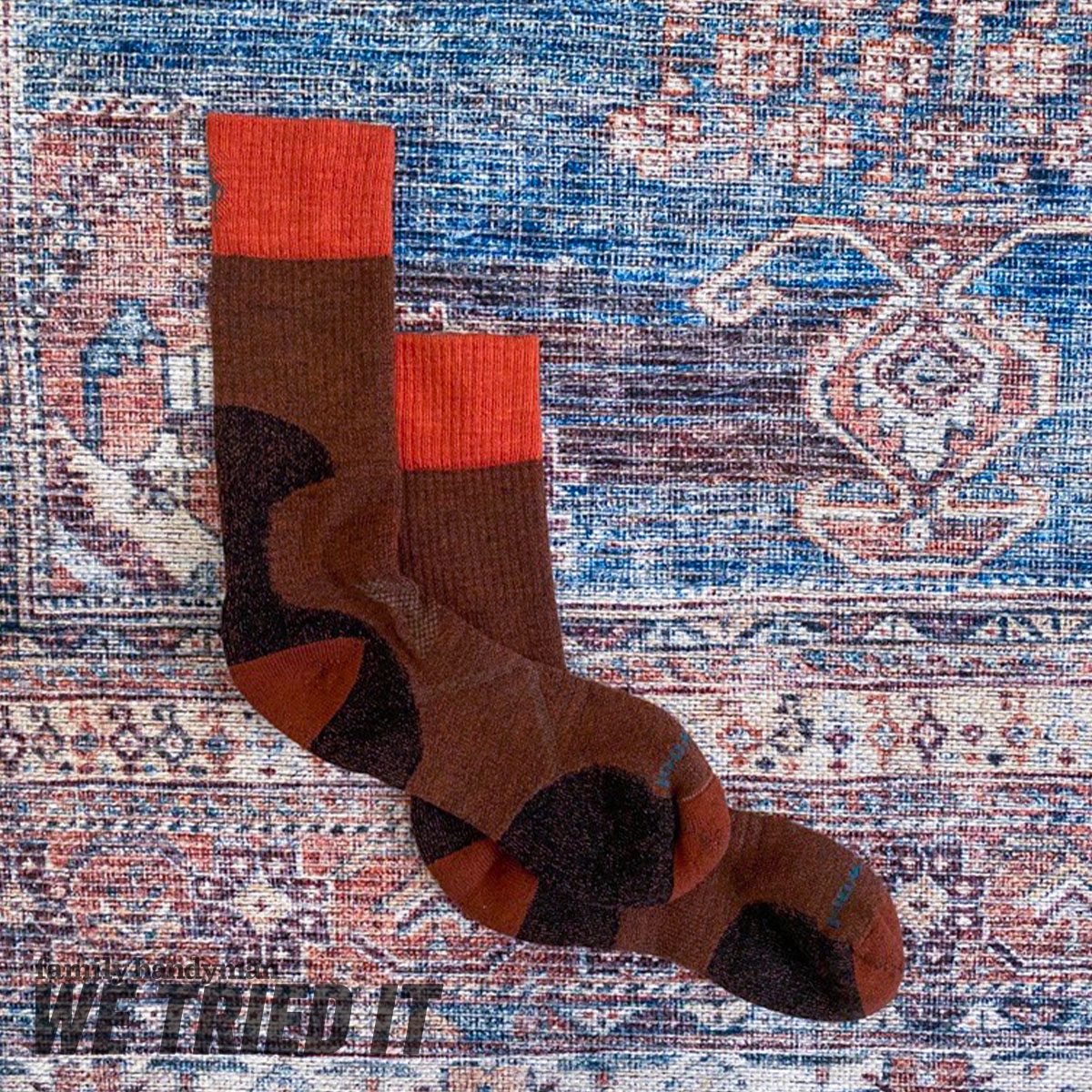 Two brown socks with red tops are arranged on a patterned rug, showcasing their design against a textured blue and red background.