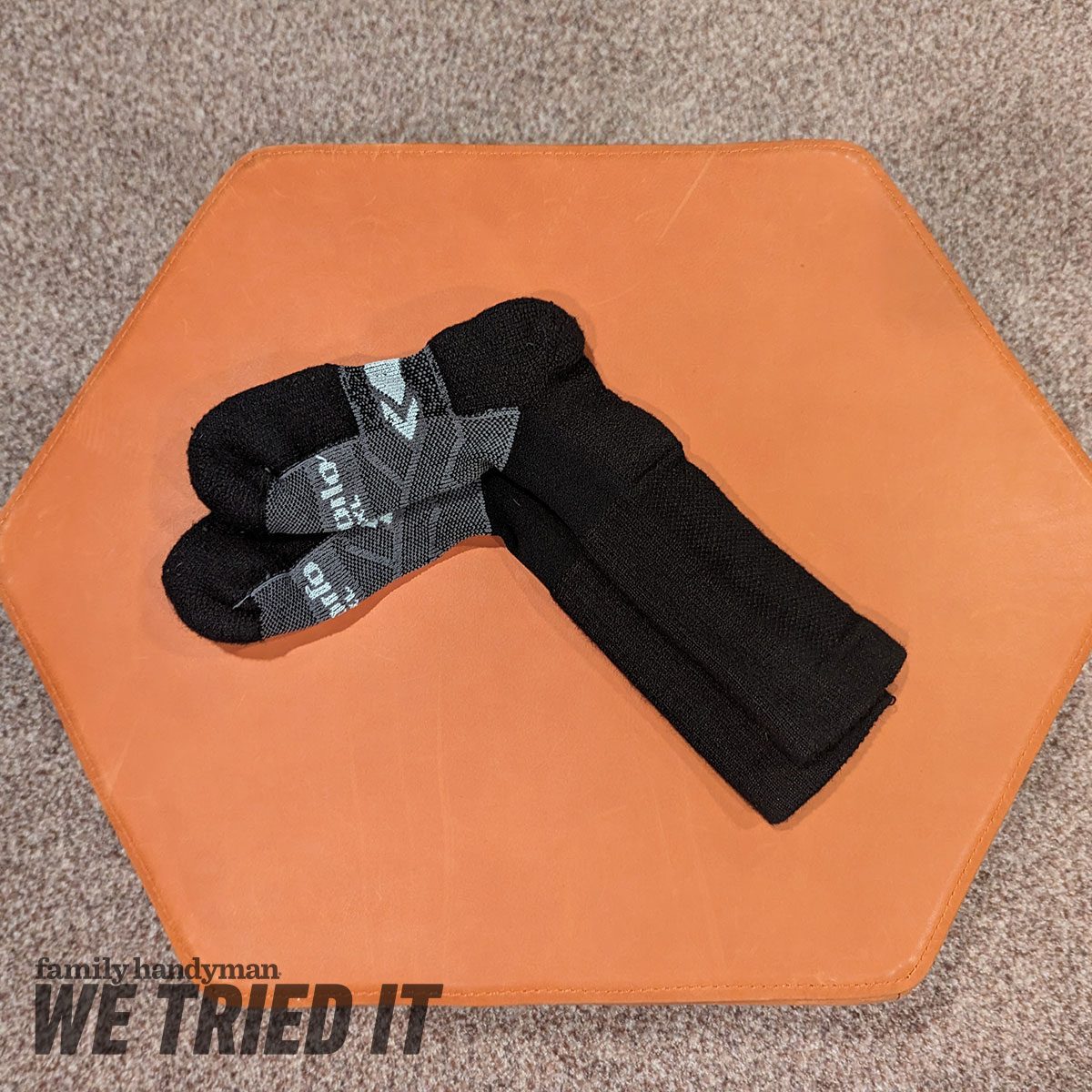 Black socks with a textured design are neatly folded on a hexagonal, orange leather surface, surrounded by a light brown carpet.