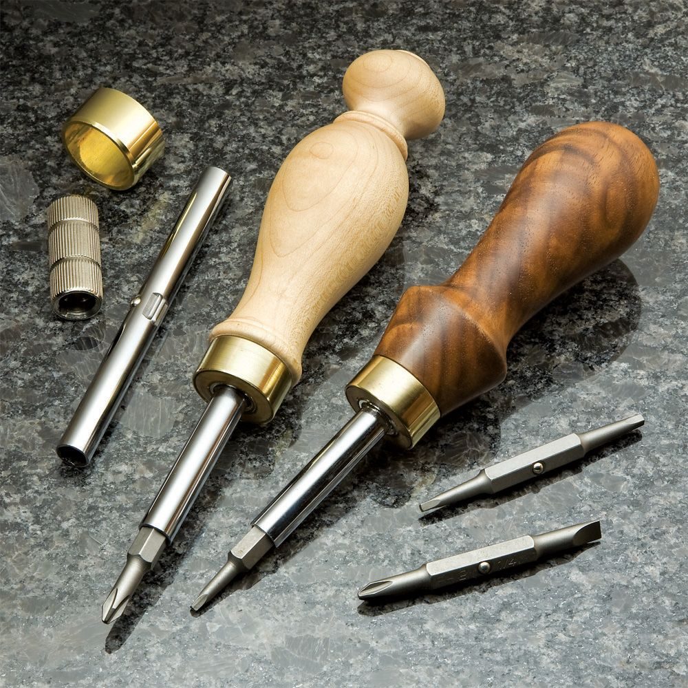 Two screwdrivers with wooden handles are resting on a dark, smooth surface, accompanied by metal attachments and various screwdriver bits nearby.