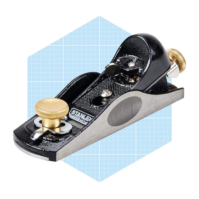 A hand plane rests on a light blue grid background, featuring a smooth metal base and gold knobs, used for shaping wood surfaces.