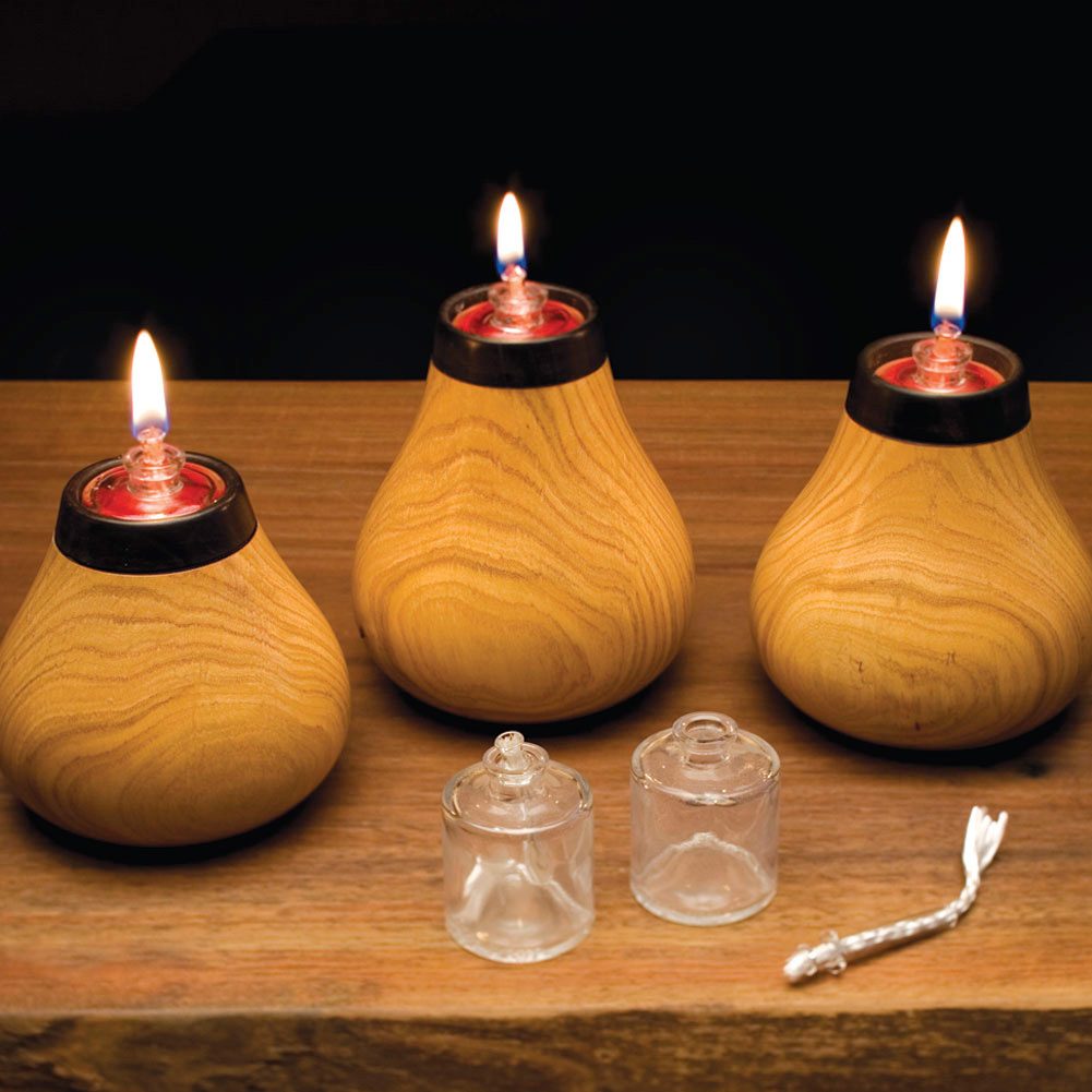 Three wooden lamps with flames are positioned on a wooden surface, accompanied by two glass components and a thin, braided cord, against a dark background.