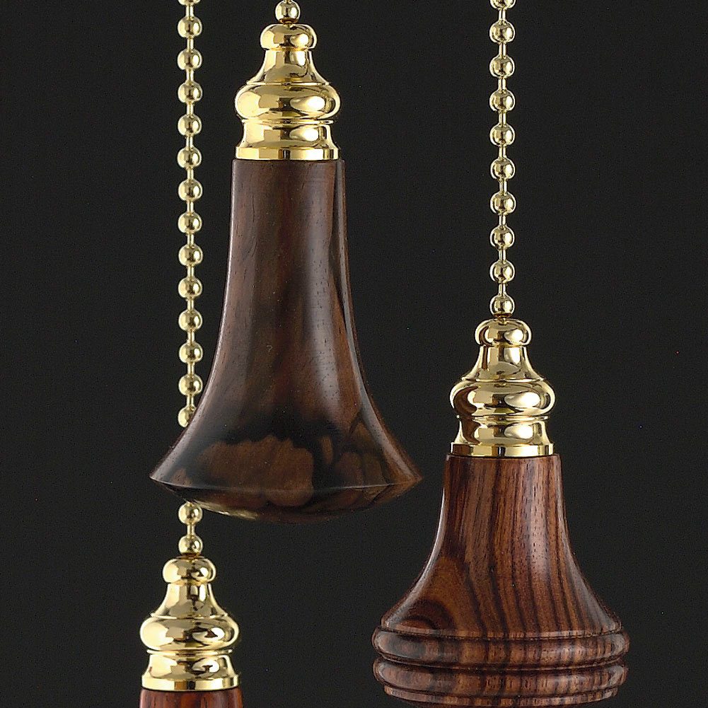 Three decorative wooden pull chains hang downwards, featuring ornate golden tops, against a black background. The chains connect to the wooden elements.