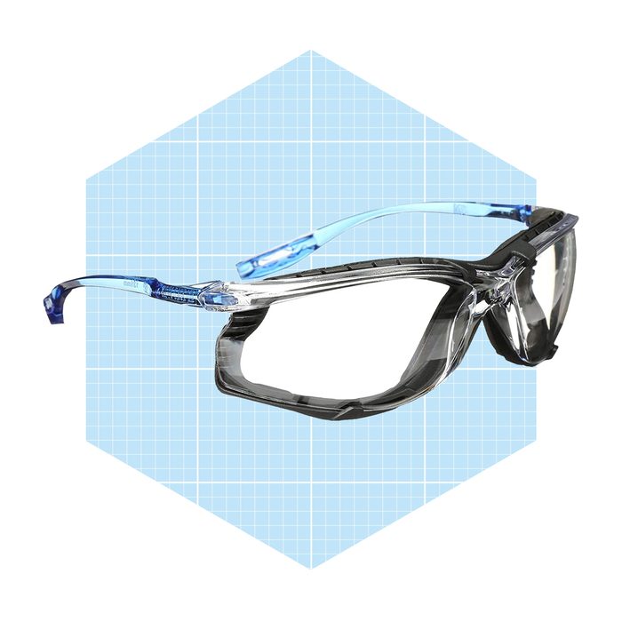 Safety glasses are positioned prominently, showcasing their sleek design against a light blue grid background. The lenses appear clear and protective.