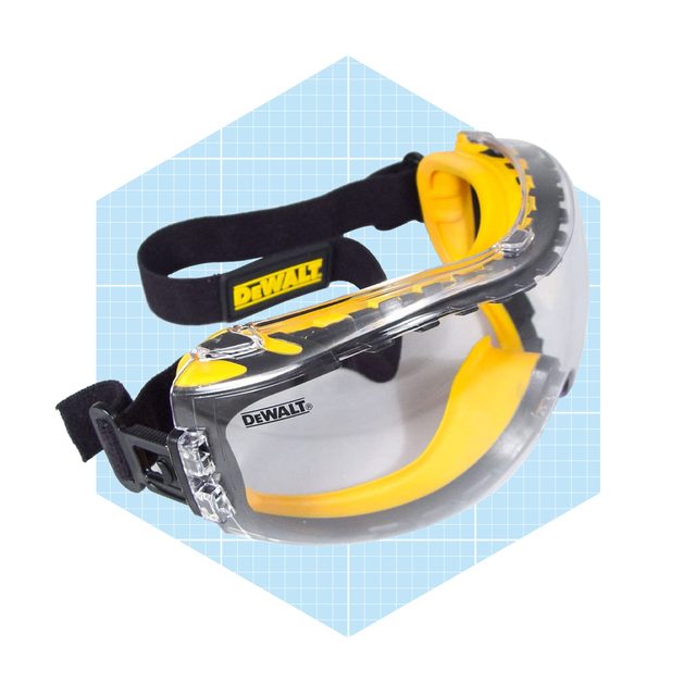 Protective goggles with a clear shield and yellow accents rest against a light blue geometric background, designed for safety during construction or industrial activities.