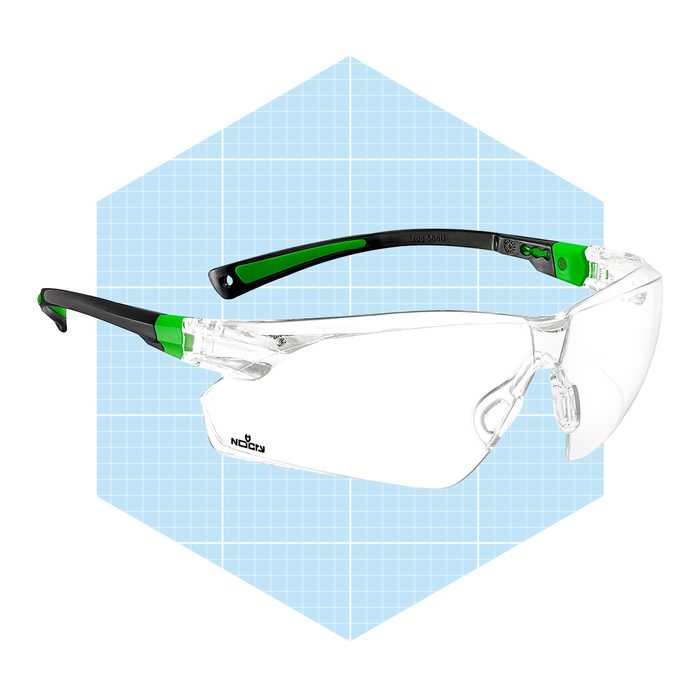 Safety glasses with clear lenses and green accents rest against a light blue grid, designed for protection during work or sports activities.