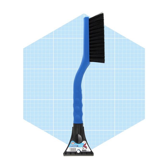 A blue-handled brush with stiff bristles stands upright against a light blue grid background, designed for cleaning surfaces or removing debris.