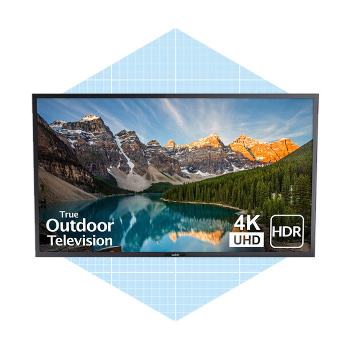 A television displays a scenic landscape of mountains and a lake, emphasizing its features as a true outdoor model with 4K UHD and HDR capabilities.