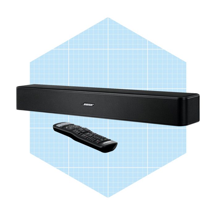 A black soundbar sits horizontally with a remote control below it, against a blue grid-pattern background, suggesting a modern audio setup.
