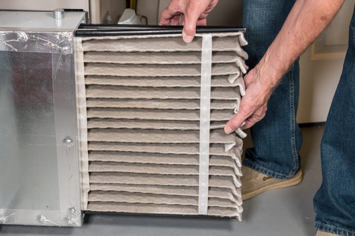 A person removes a thick, folded air filter from a metal housing in a home environment, preparing for maintenance or replacement.