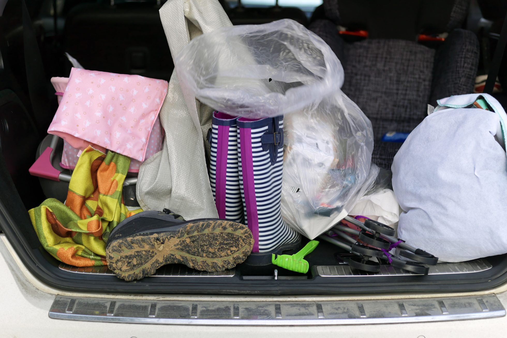 An assortment of items, including boots, bags, and a blanket, clutter the trunk of a car, suggesting preparation for an outdoor activity.