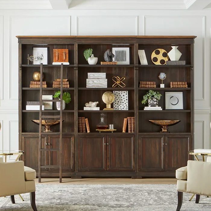 A wooden bookshelf displays various decorative items and books, while a ladder leans against it in a stylish, well-lit room with neutral tones.