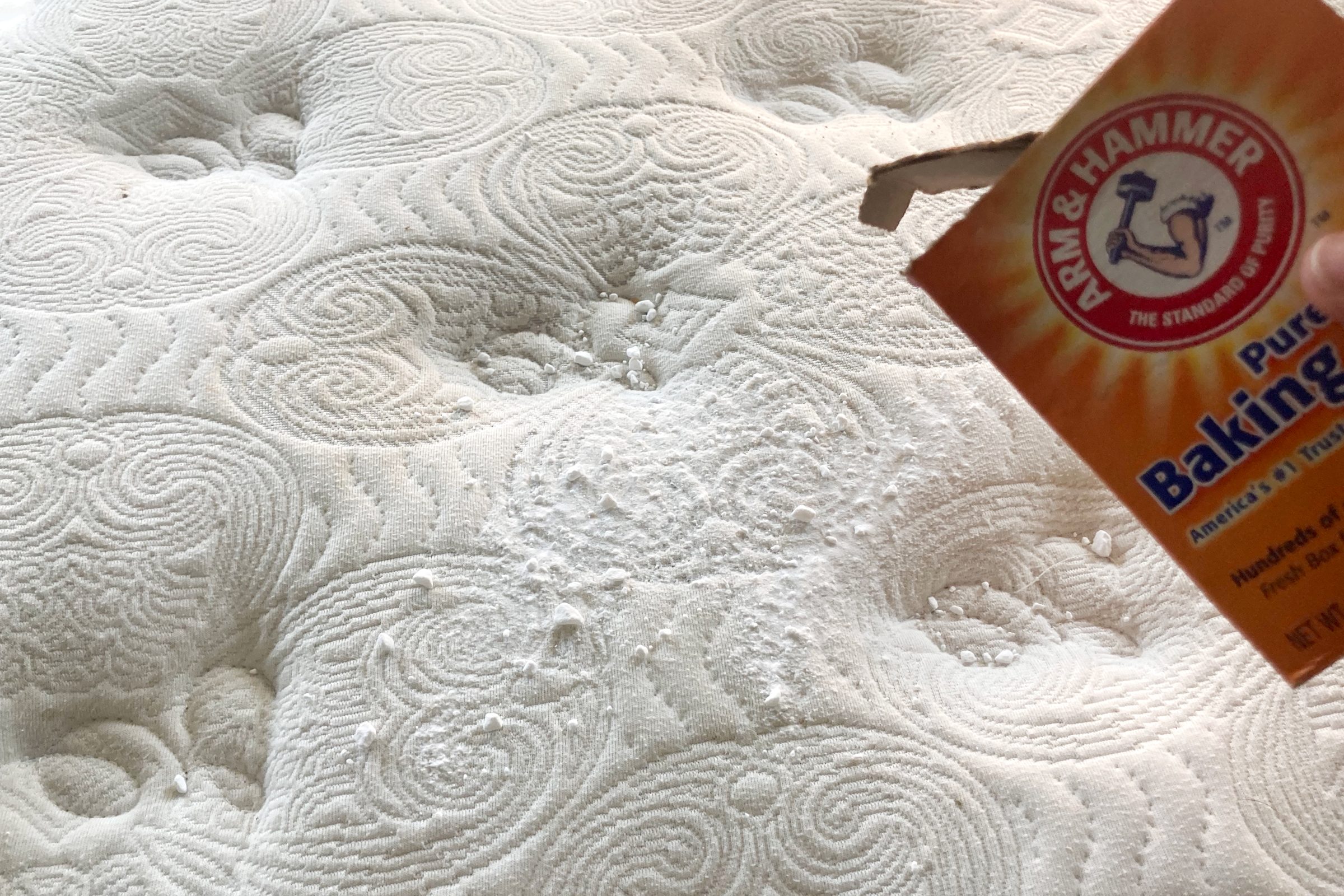 sprinkling baking soda on a mattress