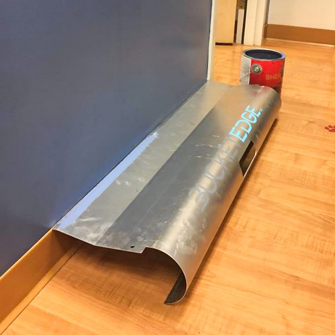A metal molding piece is resting against a wall, with paint can nearby, indicating preparation for finishing touches in a room with wooden flooring.