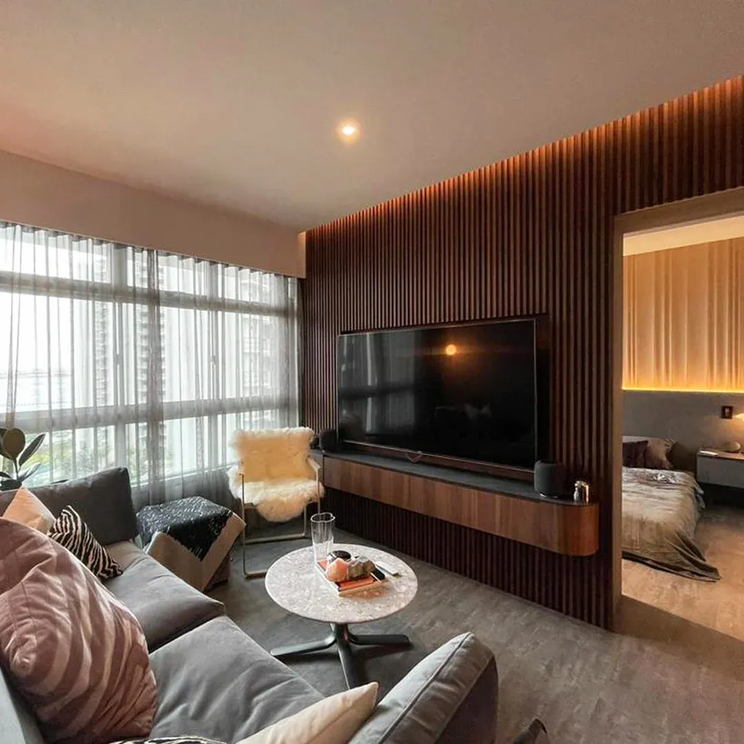 A modern living room features a gray sofa facing a sleek TV. A round table holds drinks, with large windows providing natural light and a cozy atmosphere.