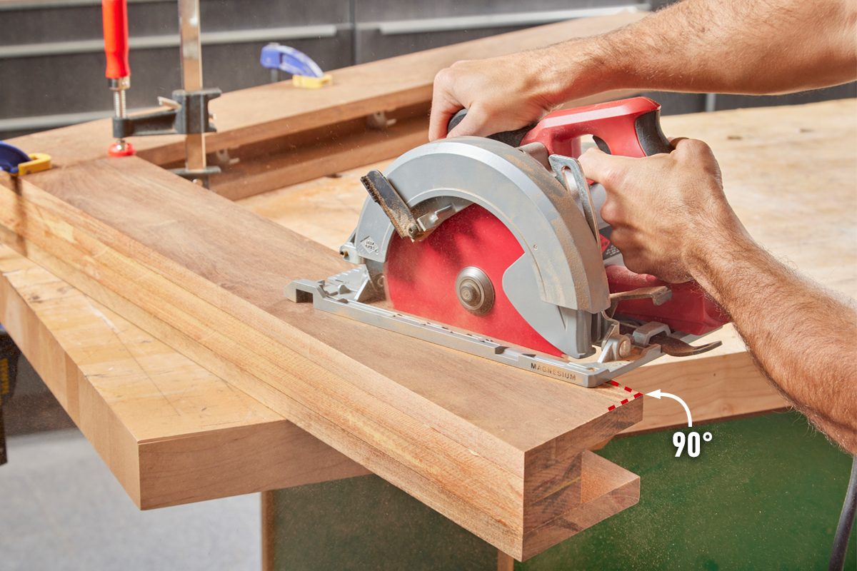 A circular saw cuts through a wooden plank held on a workbench, with sawdust flying around in a well-equipped workshop.