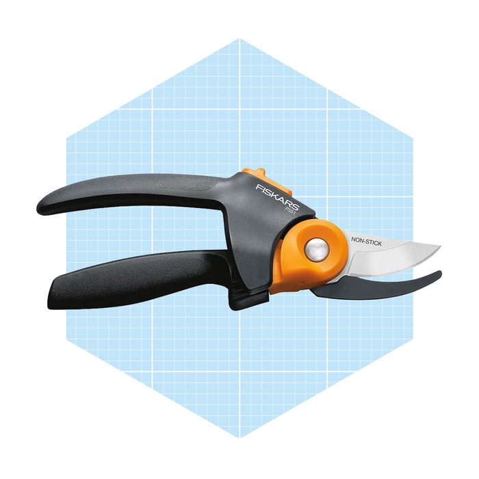 A pair of Fiskars non-stick pruning shears rests against a light blue grid background, designed for cutting plants with efficiency and ease.