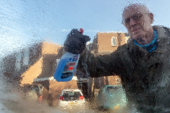 Senior de icing his car window with a bottle of antifreeze spray .