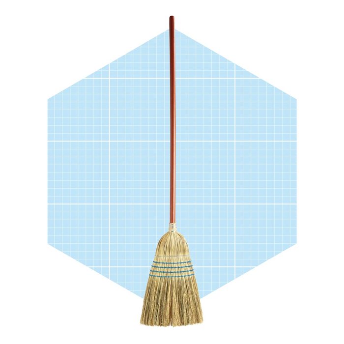 A broom stands upright, ready for use, against a light blue grid-patterned background, suggesting a clean, organized environment.