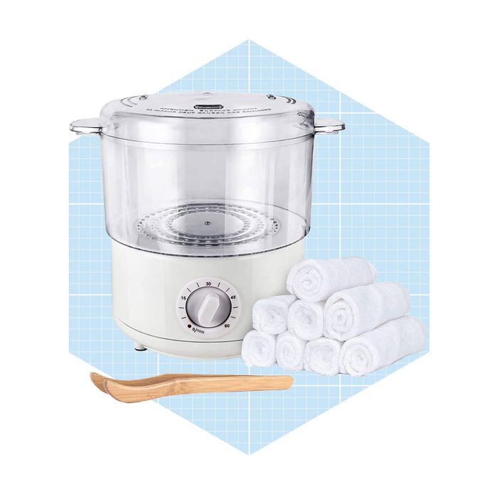 A steam towel warmer stands beside neatly rolled white towels and a wooden tong. It