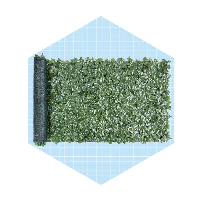 A roll of artificial green leafy material is partially unrolled on a light blue grid background, intended for decoration or coverage.