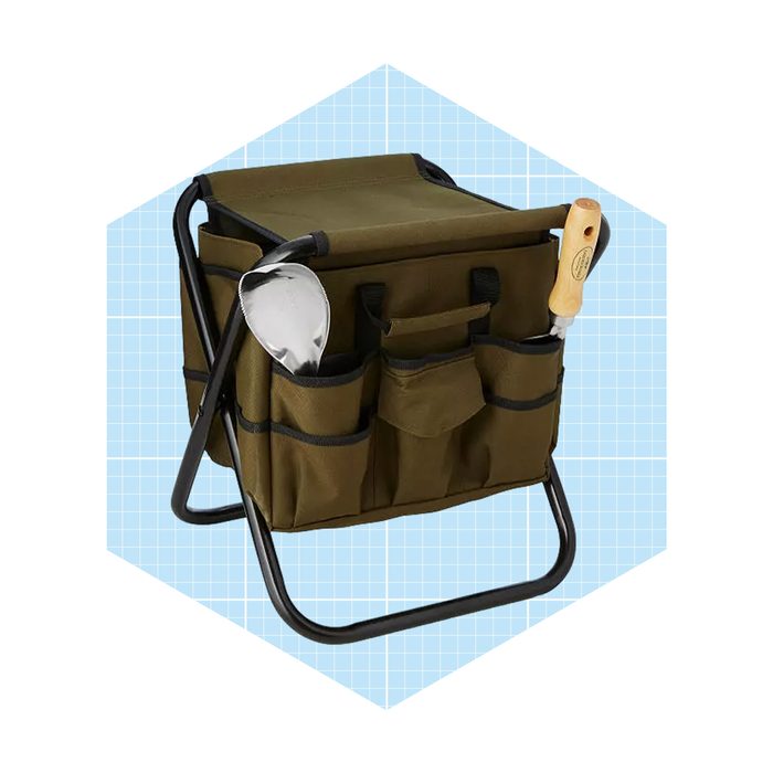 A sturdy, green gardening tote sits on a black frame, featuring pockets and tools like a trowel, set against a light blue grid background.