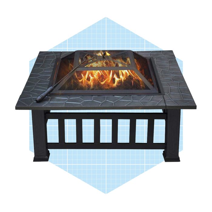 A square fire pit features a mesh cover containing flames, with a poker resting nearby, set against a light blue geometric background.